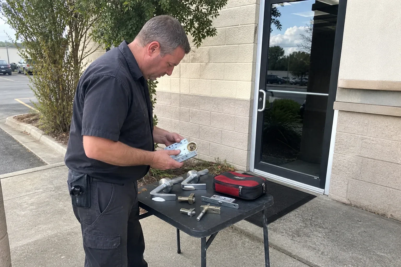 Technician examining detached commercial lock hardware on a table outside a shop entrance. — Business Lockout Service, St. Catharines