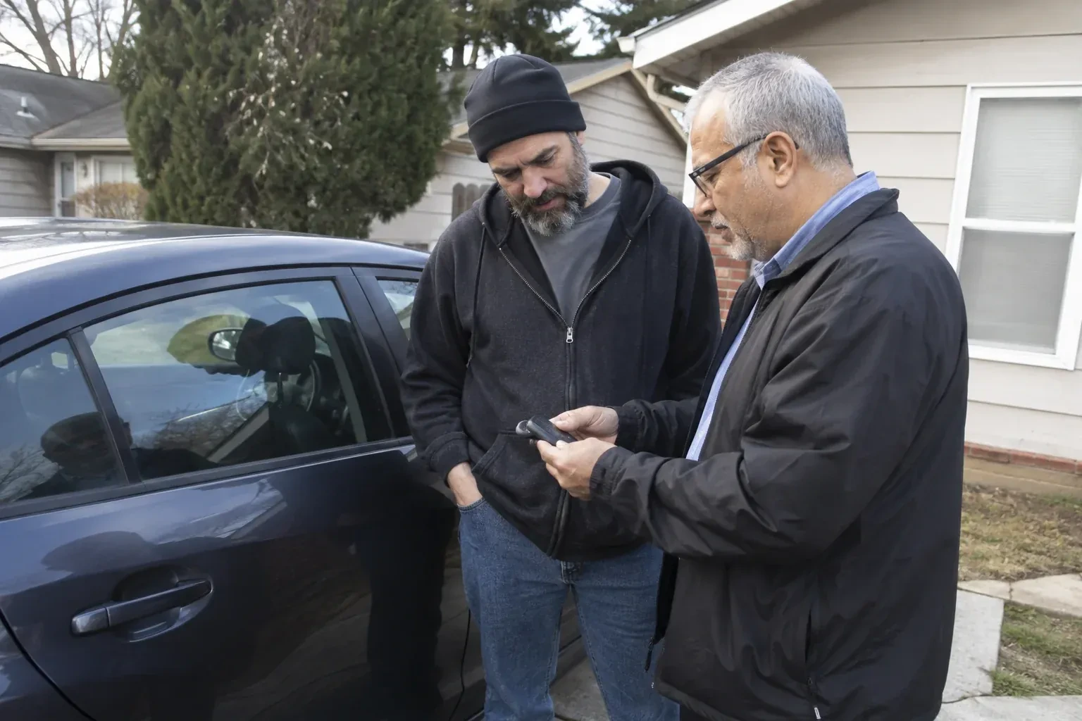 Two adults discussing a key fob beside a parked car. — Car Lockout Service, St. Catharines