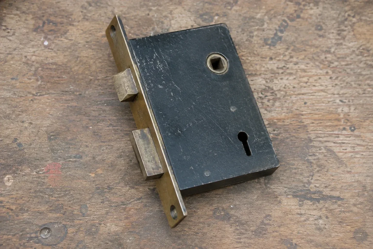 Closed mortise lock case with spindle opening, keyhole, latch and deadbolt on a wooden workbench. — Vintage Mortise Lock Service, St. Catharines