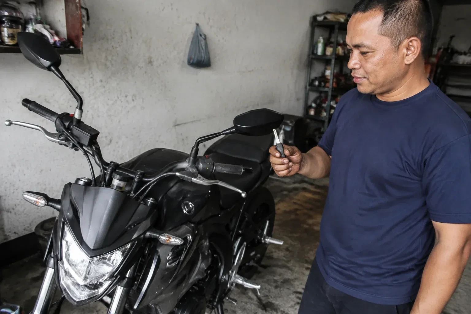 Person holding a key beside a black motorcycle in a garage. — Motorcycle & Scooter Keys, St. Catharines